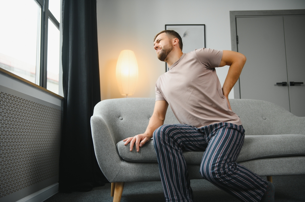 Man on sofa holding his lower back in pain from kidney stones in Los Angeles, CA